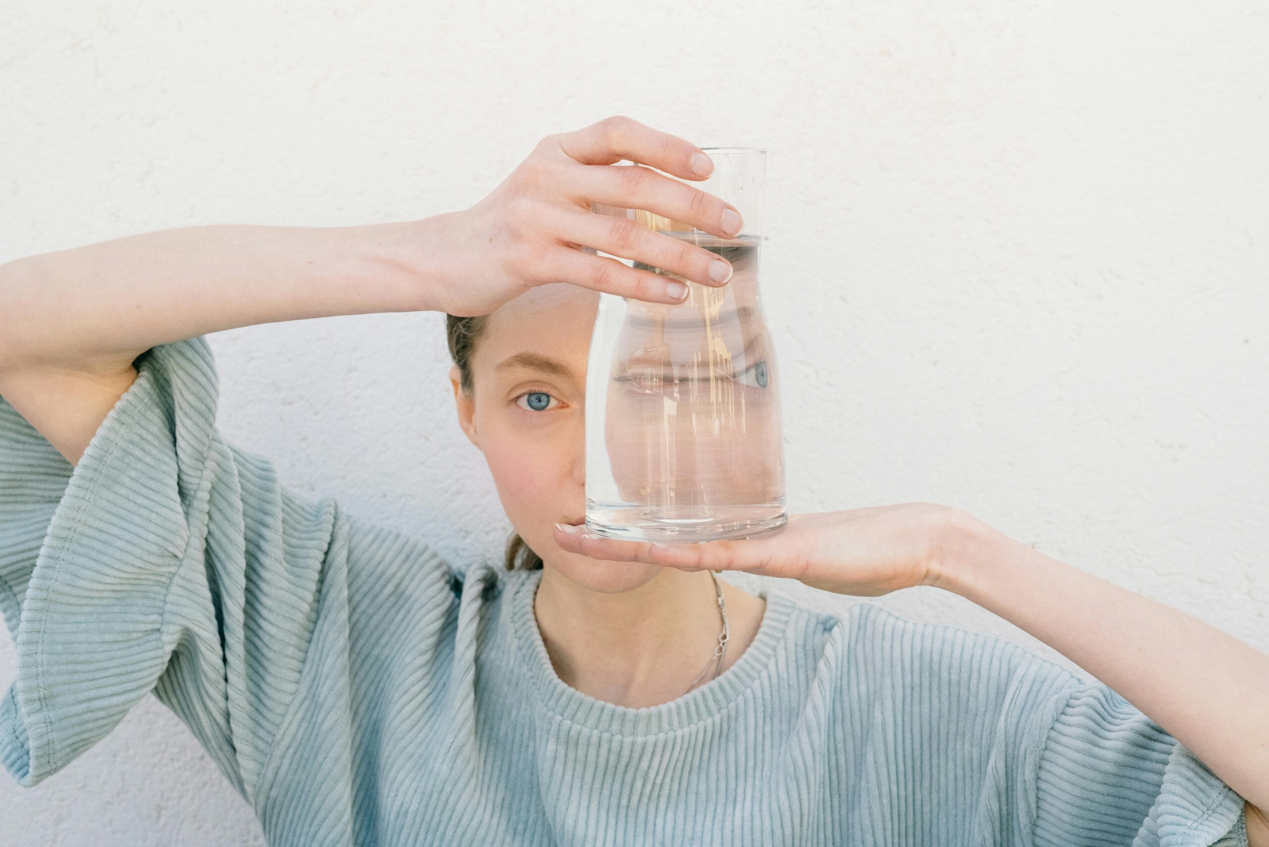 Woman holding a glass jug reflecting her face, creating a unique visual distortion.