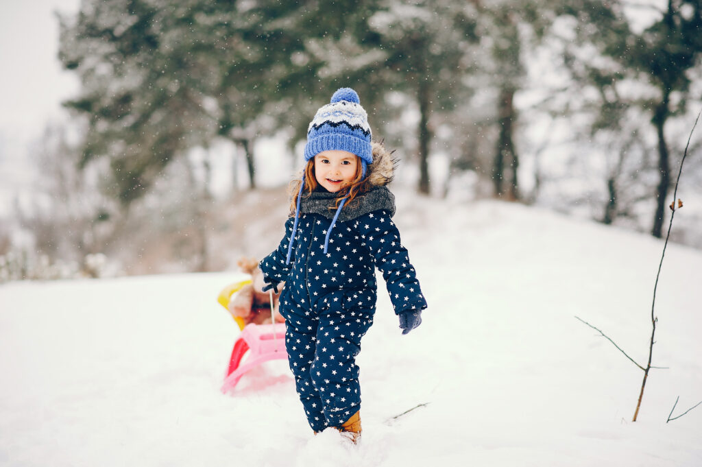 little girl in a blue hat playing in a winter forest